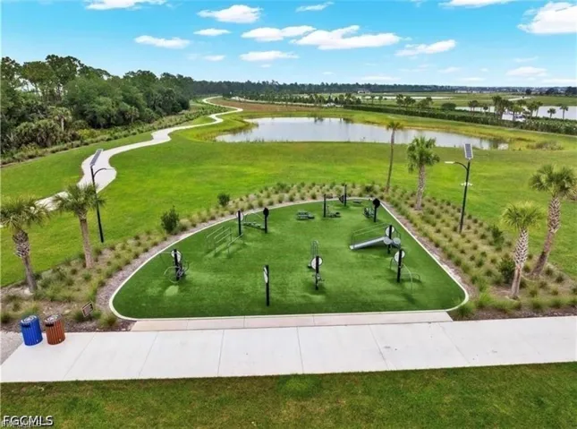 Outdoor fitness area with artificial turf, surrounded by lush green landscaping, a paved walking path, and mature palm trees