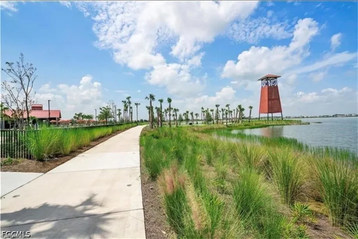 Paved pathway bordered by manicured landscaping, featuring mature palm trees and a prominent water tower structure