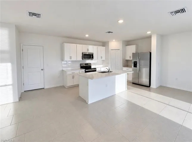 White shaker cabinetry, stainless steel appliances, central kitchen island with seating, polished tile flooring, and recessed lighting