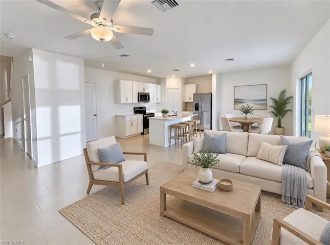 Spacious open-concept layout featuring light-toned flooring, a modern kitchen with white cabinetry, stainless steel appliances, and an island with bar seating