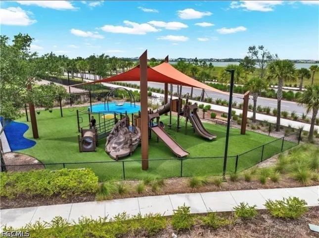 Fenced playground area featuring multiple slides, climbing elements, and a shade structure over artificial turf