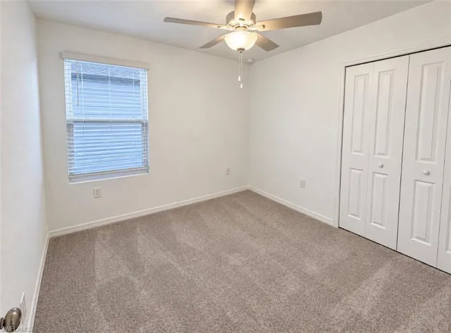 Neutral-toned carpet flooring, a window with blinds, a ceiling fan with integrated lighting, and white bi-fold closet doors