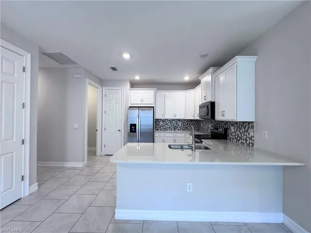 Kitchen featuring white cabinetry, light stone counters, stainless steel appliances, decorative backsplash, and light tile patterned floors