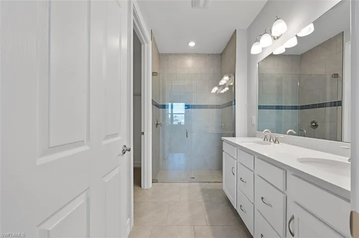 Full bath with double vanity, a stall shower, light tile patterned floors, and recessed lighting
