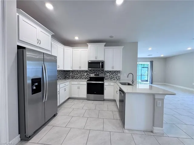 Kitchen featuring stainless steel appliances, decorative backsplash, white cabinetry, a peninsula, and light stone countertops