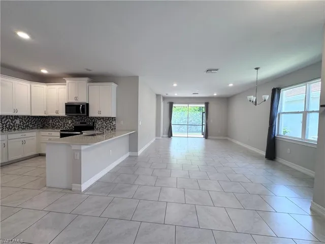 Kitchen with stainless steel appliances, decorative backsplash, white cabinets, open floor plan, and recessed lighting
