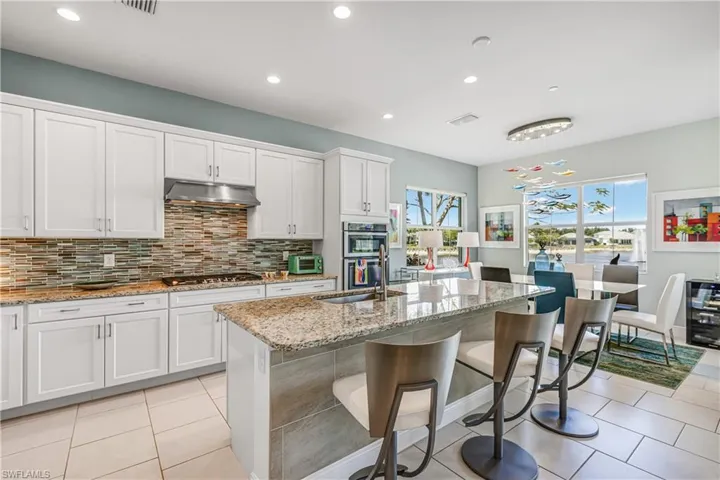 Kitchen featuring light stone counters, white cabinets, a kitchen island with sink, recessed lighting, and a kitchen breakfast bar