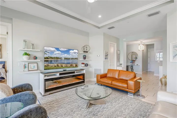 Living room with light tile patterned floors, crown molding, a ceiling fan, and a raised ceiling