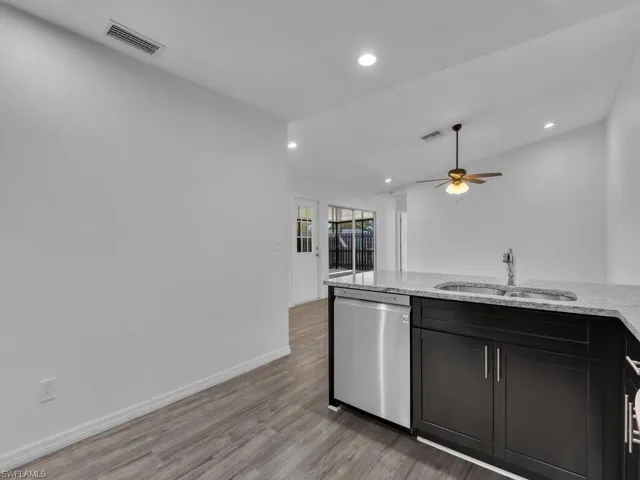 Kitchen with stainless steel dishwasher, light stone counters, light wood-style flooring, ceiling fan, and dark cabinetry