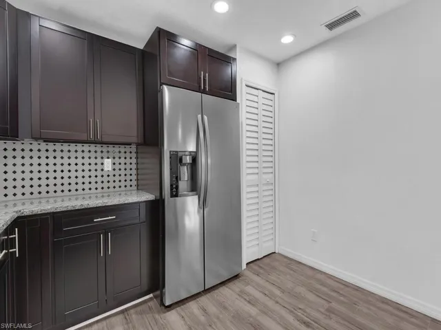 Kitchen featuring stainless steel fridge, light stone counters, dark wood finish cabinetry, light wood-style flooring, and recessed lighting