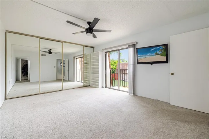 Carpeted interior space featuring full-wall mirrored closet doors with gold-tone framing, a ceiling fan with integrated lighting, and a sliding glass door opening to a private balcony