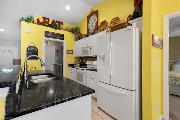 Kitchen featuring tasteful backsplash, white cabinets, light tile patterned floors, white appliances, and sink
