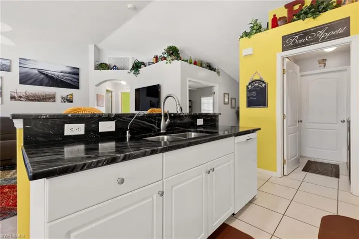 Kitchen with white cabinets, light tile patterned floors, sink, and vaulted ceiling