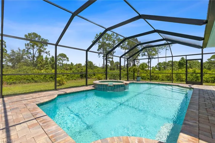 View of pool featuring glass enclosure, a patio, and an in ground hot tub