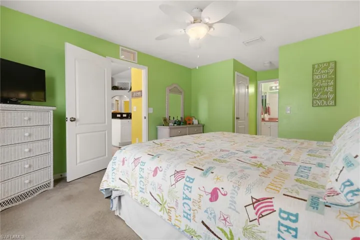 Bedroom with ensuite bathroom, light carpet, and ceiling fan