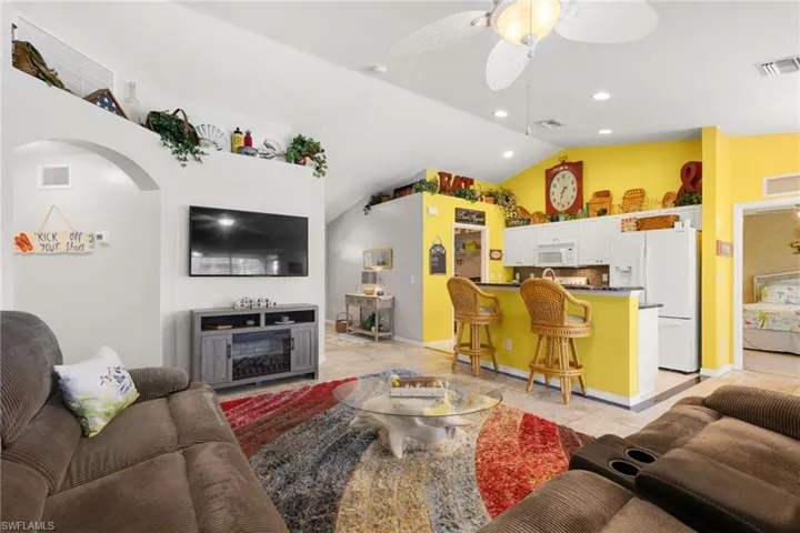 Tiled living room with ceiling fan, a fireplace, and vaulted ceiling
