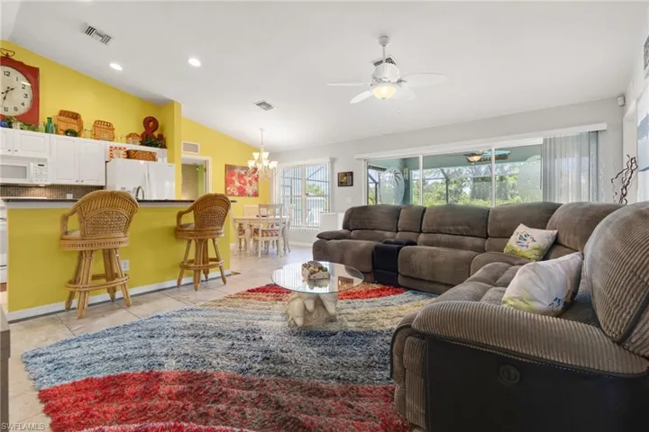 Tiled living room with ceiling fan with notable chandelier and vaulted ceiling