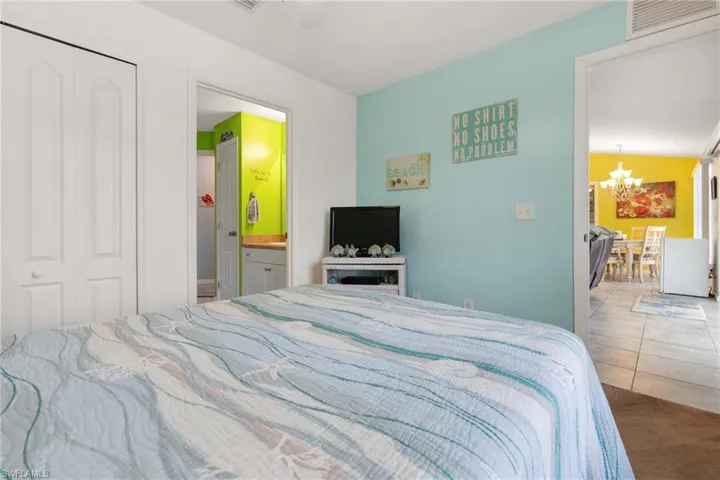 Bedroom with light tile patterned floors, ensuite bath, ceiling fan with notable chandelier, and a closet
