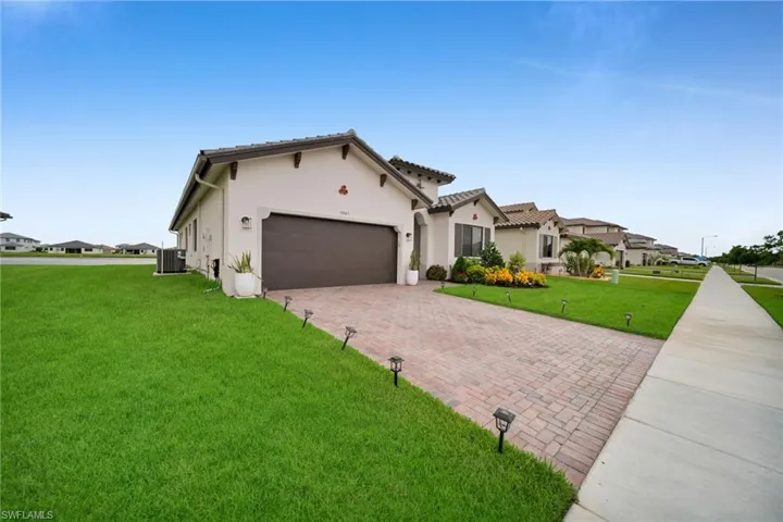 Contemporary stucco exterior with a tiled roof, paver driveway, and an integrated garage