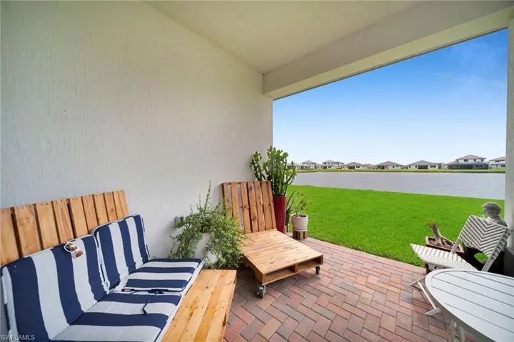 Covered patio featuring a brick paver floor, stucco walls, and a substantial water feature beyond a manicured lawn