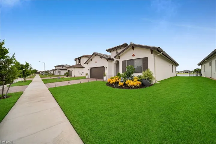 Exterior stucco facade with a tile roof, featuring a paver driveway, a manicured lawn, and mature landscaping