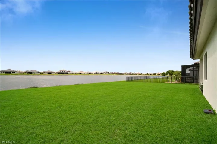 Expansive green lawn bordering a sizable body of water, featuring a black perimeter fence and screened enclosure