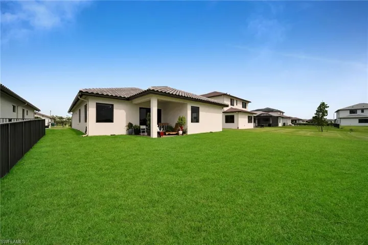 Expansive green lawn bordering a single-story residence with a covered patio, dark-framed windows, and a tiled roof