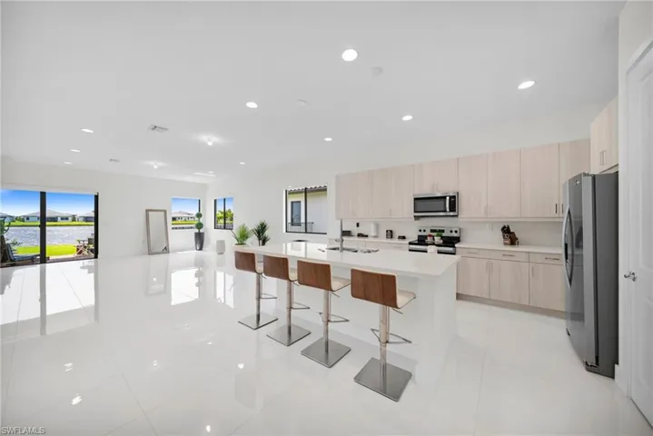 Spacious open-concept kitchen and living area featuring white tile flooring, recessed lighting, and a kitchen island with seating