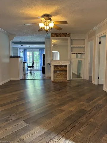 Unfurnished living room with crown molding, a textured ceiling, a ceiling fan, and dark wood-style floors.