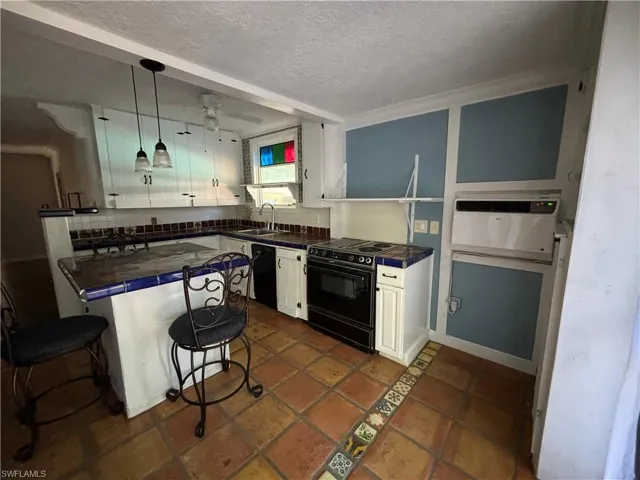 Kitchen featuring white cabinets, tile counters, decorative light fixtures, black appliances, and a textured ceiling.