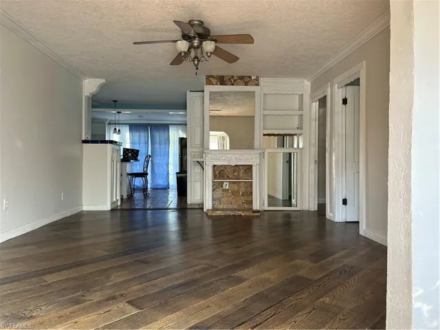 Unfurnished living room with a textured ceiling, crown molding, ceiling fan, dark wood finished floors, and a textured wall.