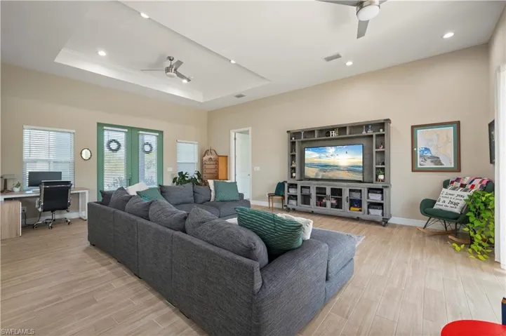 Living area featuring light wood finished floors, a ceiling fan, a tray ceiling, baseboards, and recessed lighting