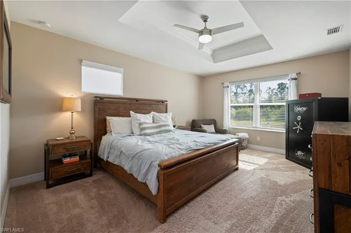 Bedroom with a tray ceiling, baseboards, visible vents, crown molding, and light colored carpet