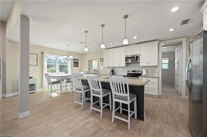 Kitchen with light wood finished floors, white cabinetry, baseboards, appliances with stainless steel finishes, and light stone counters