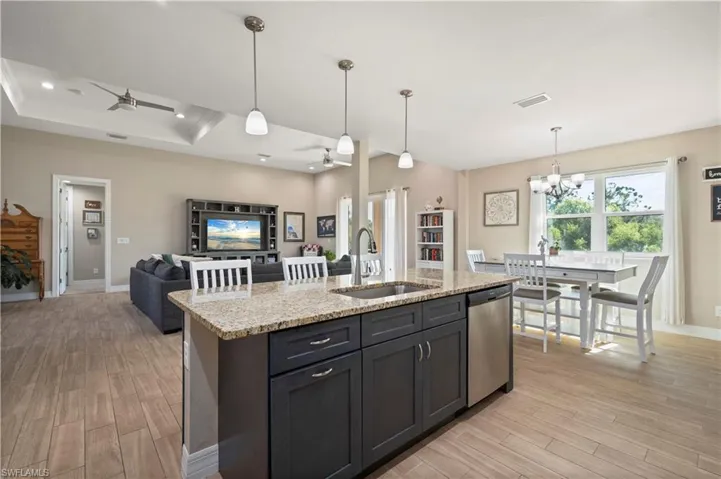 Kitchen with light wood-type flooring, stainless steel dishwasher, light stone counters, and a sink