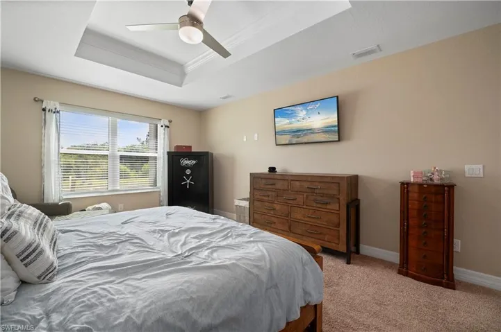 Bedroom with ornamental molding, ceiling fan, light carpet, a tray ceiling, and baseboards