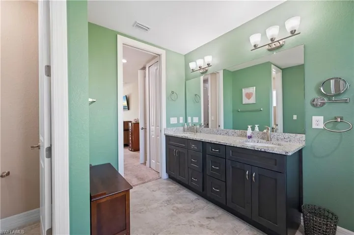 Full bath with a textured wall, visible vents, a sink, and double vanity
