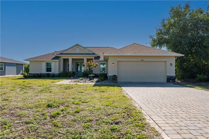 Ranch-style home with a garage, stucco siding, a front lawn, and decorative driveway