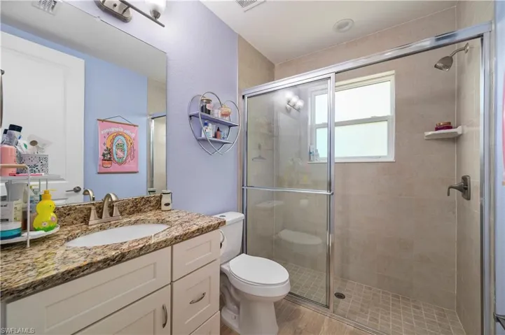 Bathroom with toilet, wood finished floors, vanity, visible vents, and a shower stall