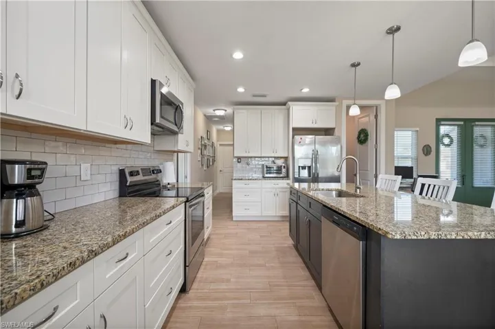 Kitchen featuring a sink, appliances with stainless steel finishes, white cabinets, hanging light fixtures, and light wood-style floors
