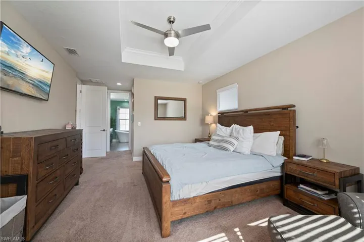 Bedroom featuring a tray ceiling, light carpet, a ceiling fan, and visible vents