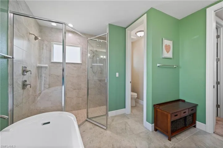 Bathroom featuring a soaking tub, toilet, baseboards, and a shower stall