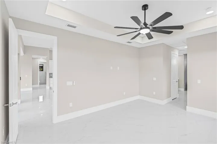 Empty room with light marble finish flooring, a raised ceiling, a ceiling fan, and recessed lighting