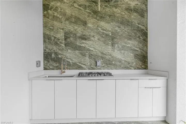 Detailed view of wet bar, stainless steel gas stovetop, and a textured wall