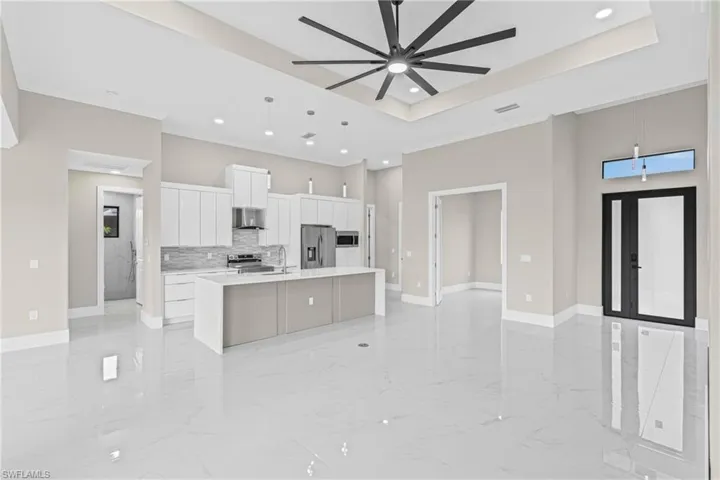 Kitchen with open floor plan, white cabinetry, decorative light fixtures, a kitchen island with sink, and stainless steel appliances