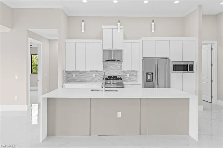 Kitchen with light marble finish floors, light stone countertops, stainless steel appliances, decorative backsplash, and ornamental molding