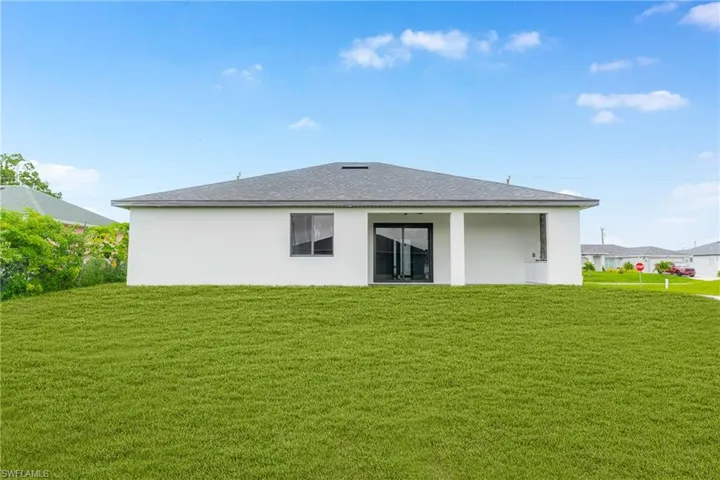 Back of property with a lawn, stucco siding, and a shingled roof