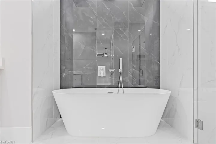 Full bathroom with a freestanding bath, stone wall, marble tiled floors, and a marble finish shower