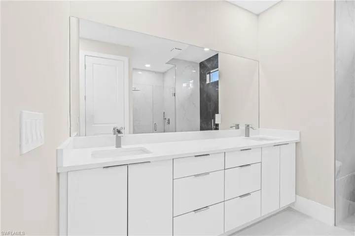 Full bathroom with a marble finish shower, double vanity, and light marble finish floors