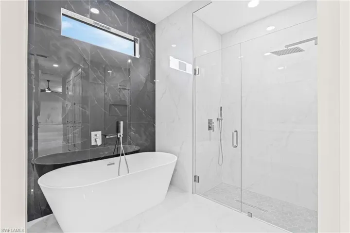Full bath with stone wall, marble tiled floors, a freestanding tub, a marble finish shower, and tile walls